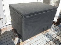 Full view of black rectangular synthetic wicker deck box with hinged lid, placed on outdoor deck.