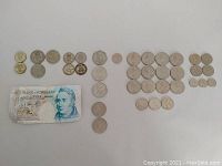 All British coins arranged in rows next to one £5 Bank of England note on a white surface