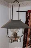 Front view of antique hanging oil lamp showing metal shade, glass chimney, and base with etched details
