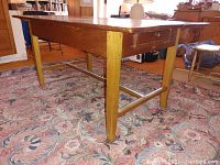 Full side view of the solid wood harvest table showing one drawer and tapered legs with wooden crossbars.