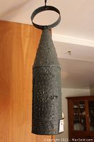Front view of tall, dark metal hanging lantern with conical top showing textured raised dot pattern and ring for hanging.