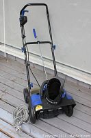 Snow Joe cordless snow blower with foldable handle, front plastic auger housing, charger cable coiled on deck