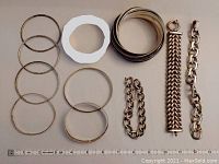Overall view of all bracelets laid out including silver bangles, chain bracelets and colored linked bangles.