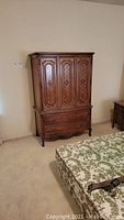 Full view of the Thomasville wood armoire showing three doors and two drawers, next to a bed.