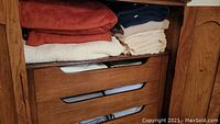 Wooden armoire drawer open showing red and white towels, cream linens folded on top.