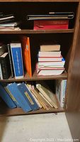 Shelf with various books including binders, hardcovers, and paperbacks, some visible wear