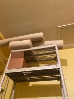 Three beige carpet rolls or remnants placed on a metal rack against a beige wall.