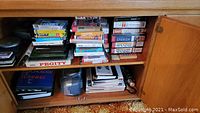 Books, VHS tapes, CDs, floppy disks and other media arranged on shelves inside a wooden cabinet. Spanish learning language tapes visible.