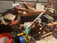 Overview of the lot showing the hose reel with hose, wooden workbench, various garden tools, black hose on rack, and other workshop items in a garage.