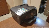 Black HP Officejet Pro 6968 printer placed on a wooden table showing front and top with some control buttons visible