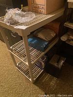 Three-tier beige plastic wire mesh shelving unit with various items stored inside, showing overall good structure but dirty and worn surfaces.