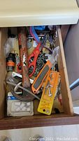 Top drawer containing hammer, scissors, utility knife, adhesive glue, screws, and miscellaneous small hardware and tools.
