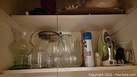 Top shelf view showing several clear glass vases and pitchers, spray starch canister, iron, and silver tray.