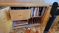 Wide shot of wooden console with open doors showing storage for vinyl records and the built-in turntable area.