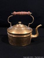 Front view of the antique brass kettle showing the turned wood handle and spout.