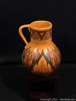 Front angle view of jug showing geometric and flame motif decoration in earthy colors under matte glaze.