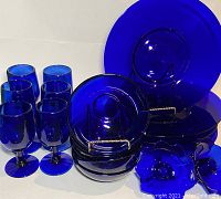 Group photo showing all cobalt blue glass dishware items including wide-rimmed shallow bowls, dessert bowls, goblets, and candlestick holders.