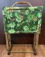 Four floral fibreglass trays nested in brass stand against wood panel background