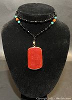 Front view of the black beaded necklace with turquoise and orange accent beads and red jade pendant on black display bust.