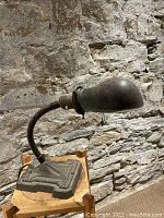 Side view of goose neck lamp showing curved neck, base and lampshade against stone wall background