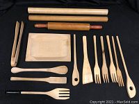 Wooden kitchen utensils laid out on black background including spatulas, forks, spoon, a small tray, and wooden tongs