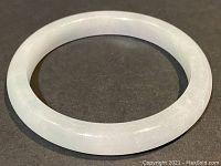 Top view of round translucent light green-white jade bangle laid flat on black background.