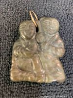 Front view of green jade pendant carved with two smiling figures, attached to a gold bale.