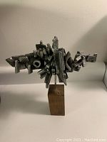 Front-side view of the abstract cast metal sculpture on a wooden stand showing detailed geometric forms and texture.