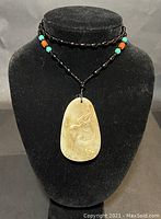Front view of necklace displayed on black bust showing the jade dragon pendant and beaded necklace with turquoise and brown accents.