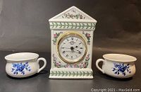 Photo showing the front view of the ceramic clock with floral decoration and the pair of cobalt blue rose miniature chamber pots placed on either side.