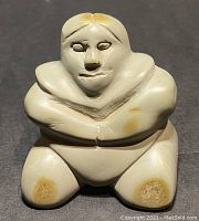 Front view of soapstone sculpture showing seated figure with arms folded.