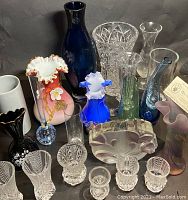 Group photo showing approximately 20 assorted glass and crystal vases in various colors including cobalt blue, pink, clear crystal with cut designs, and ruffled edges.