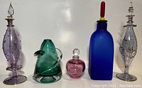 Photo of all five items in the lot showing various sized blown glass perfume bottles and a green bud vase.