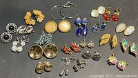 Top view of 22 assorted pairs of vintage and retro earrings in various styles and colors including blue, red, yellow, gold-tone, and silver-tone pieces