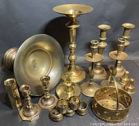 Full view of lot showing multiple brass candleholders, two footed compote bowls, a woven basket, angel bell, and set of napkin rings