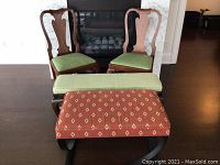 Photo showing two wooden Queen style chairs with green upholstered seats placed behind an ottoman with rust-orange diamond patterned upholstery and black metal frame.