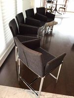 Four charcoal upholstered bar stools arranged in a row showing overall appearance and chrome frames