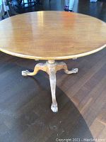 Full view of round hardwood table top and upper pedestal base showing wood finish and wear