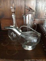 Clear glass decanter with stopper, tall cylindrical pitcher and curved ewer displayed on wooden shelf