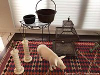 Photo showing two white vintage-style table lamps, two metal pots on a black metal side table, a birdcage in the background, and a large white pig figurine on a patterned rug.