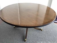 Full view of the round dining table showing the pedestal base with brass-capped legs and the wooden tabletop.