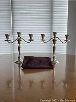 Pair of candelabras with cloth displayed on wooden table against blinds