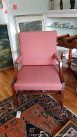 Front view of coral upholstered armchair against a wall and wooden floor.