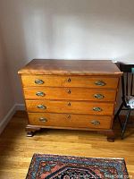 Front view of vintage wooden chest of drawers showing four drawers, brass oval handles, and keyholes. Wood finish and scratches visible.