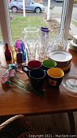 Full collection of glass bottles, drinkware, mugs, plates and decorative items on table, captured in natural window light.