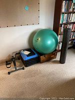 Overall view of home fitness equipment including pedal exerciser, aerobic step platforms, green exercise ball, black foam roller, and adjustable ankle weights