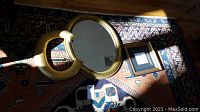 Three items on a patterned rug by hardwood floor: an oval gold-framed mirror, a metal letter C with gold distressed finish, and a small empty black picture frame.