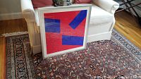 Full view of framed print leaning against sofa on patterned carpet