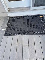 Two photos of the same black outdoor rubber mat with lattice and star pattern, placed on a gray wood deck outside a door.