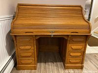 Front view of oak roll top desk showing closed tambour door and 8 drawers.